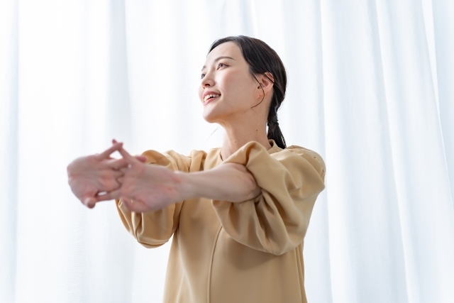 明るい部屋の中で伸びをする女性の画像