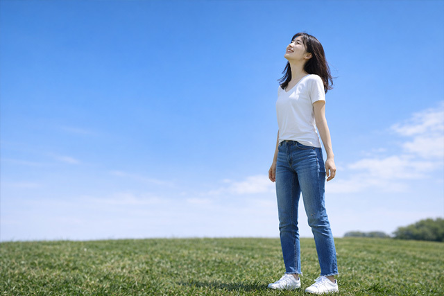 草原に一人立ち笑顔で空を見上げる女性