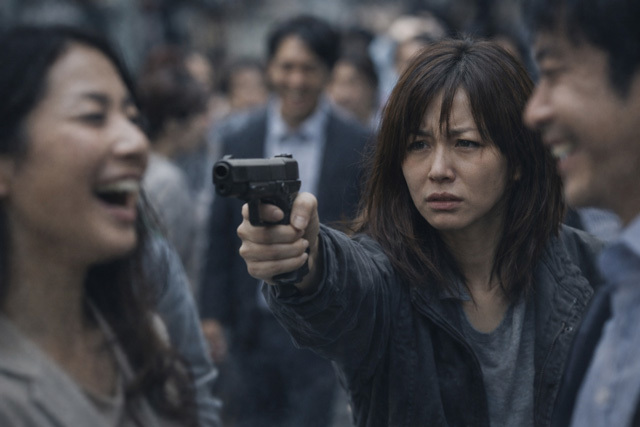 銃を向ける女性を笑う人たちの画像